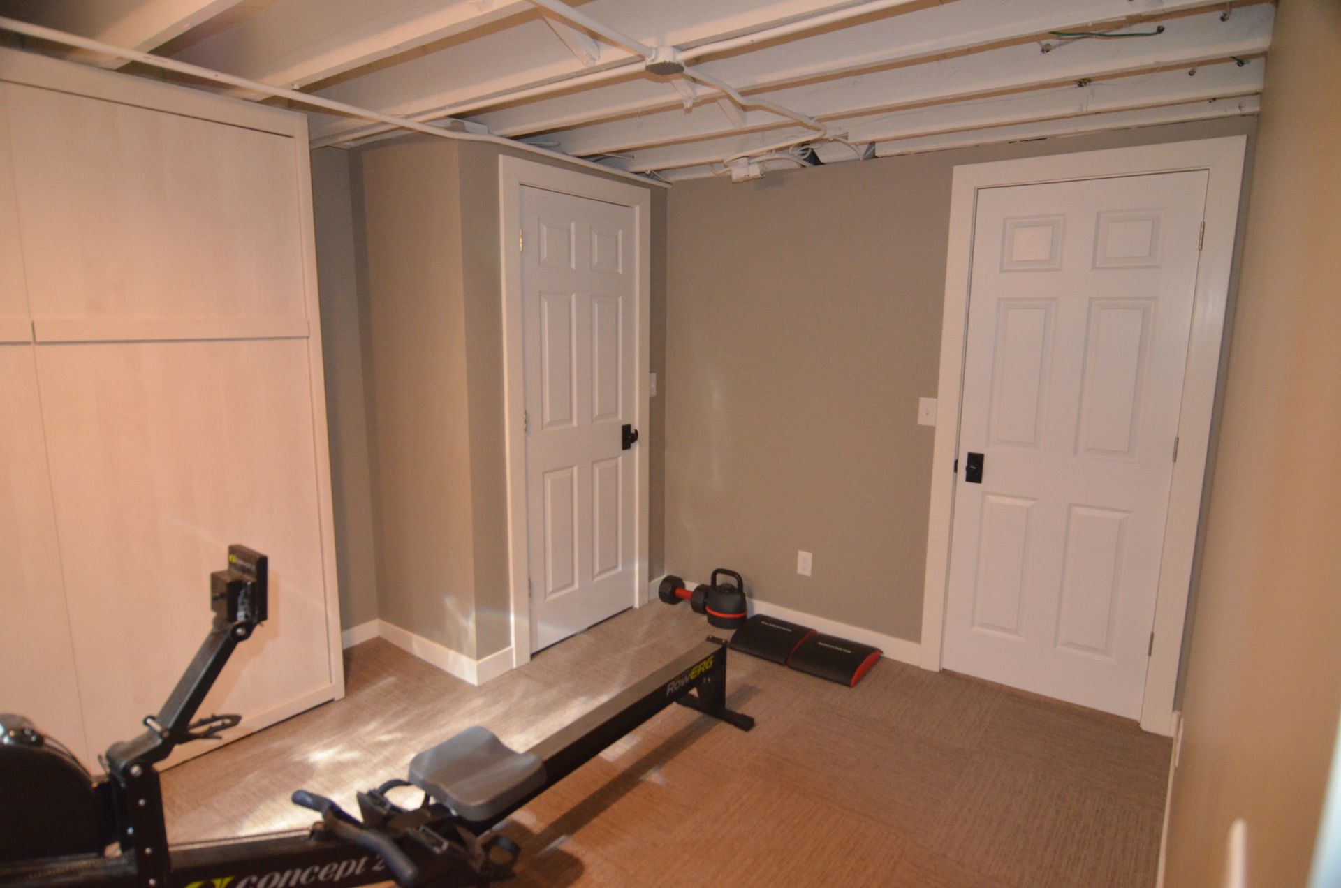 Basement gym with a rowing machine, two white doors, and beige walls.