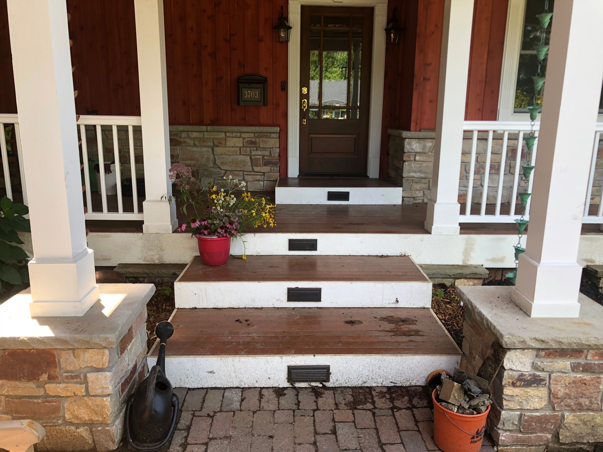 Steps leading up to a red-painted home's front door with white columns and stone accents.