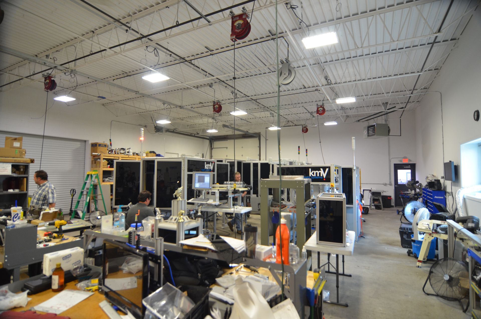 Large, well-lit workshop with numerous workstations and computer servers. People are working on electronics and machinery.