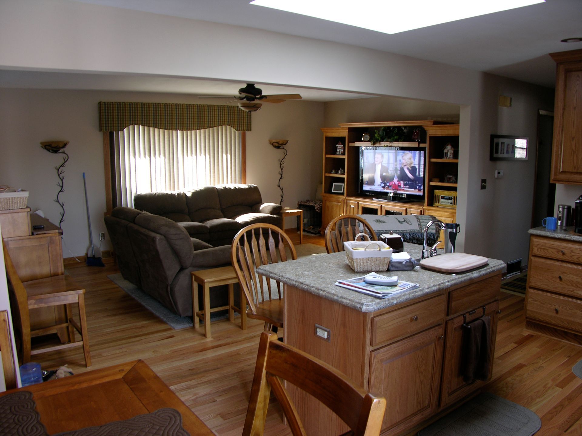 Open-concept living space with kitchen island, living area with couch, and TV entertainment center. Natural light fills the room.