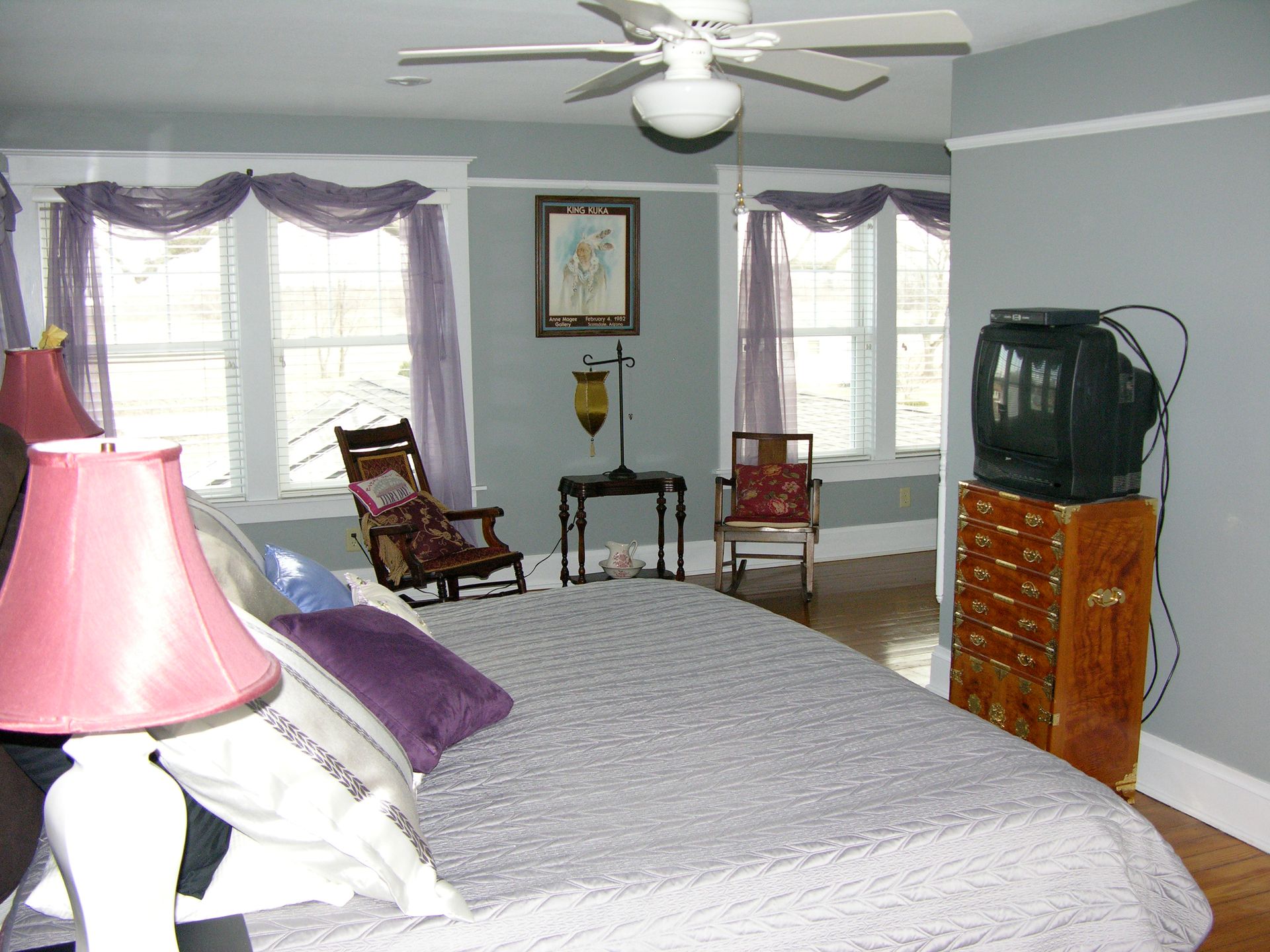 Bedroom with bed, windows, rocking chairs, and an old television on a dresser.