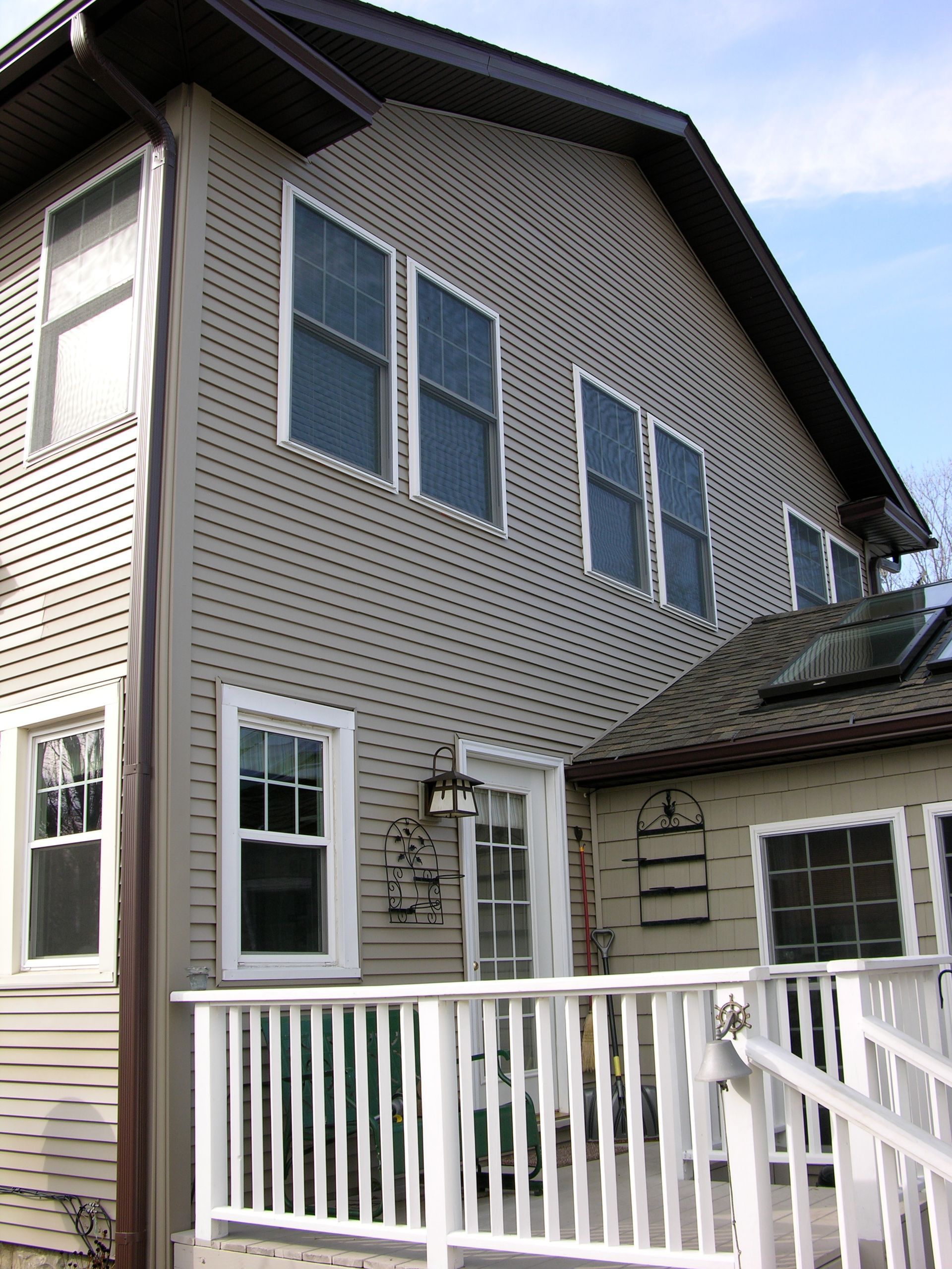 Two-story beige house with white trim. Deck with railing in the foreground. Several windows visible.