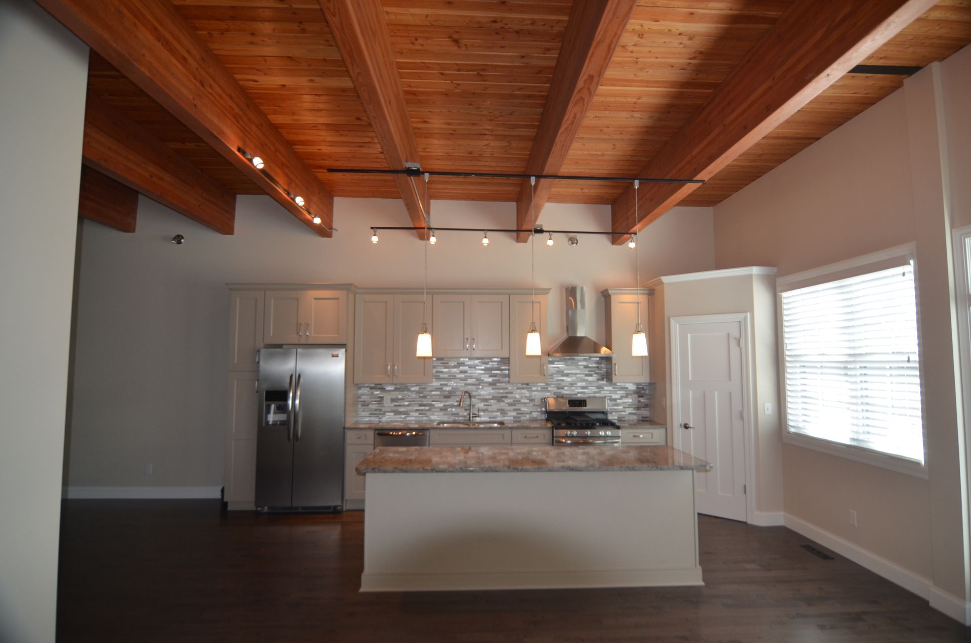 Kitchen with wood beam ceiling, stainless steel appliances, light cabinets, and a granite island.