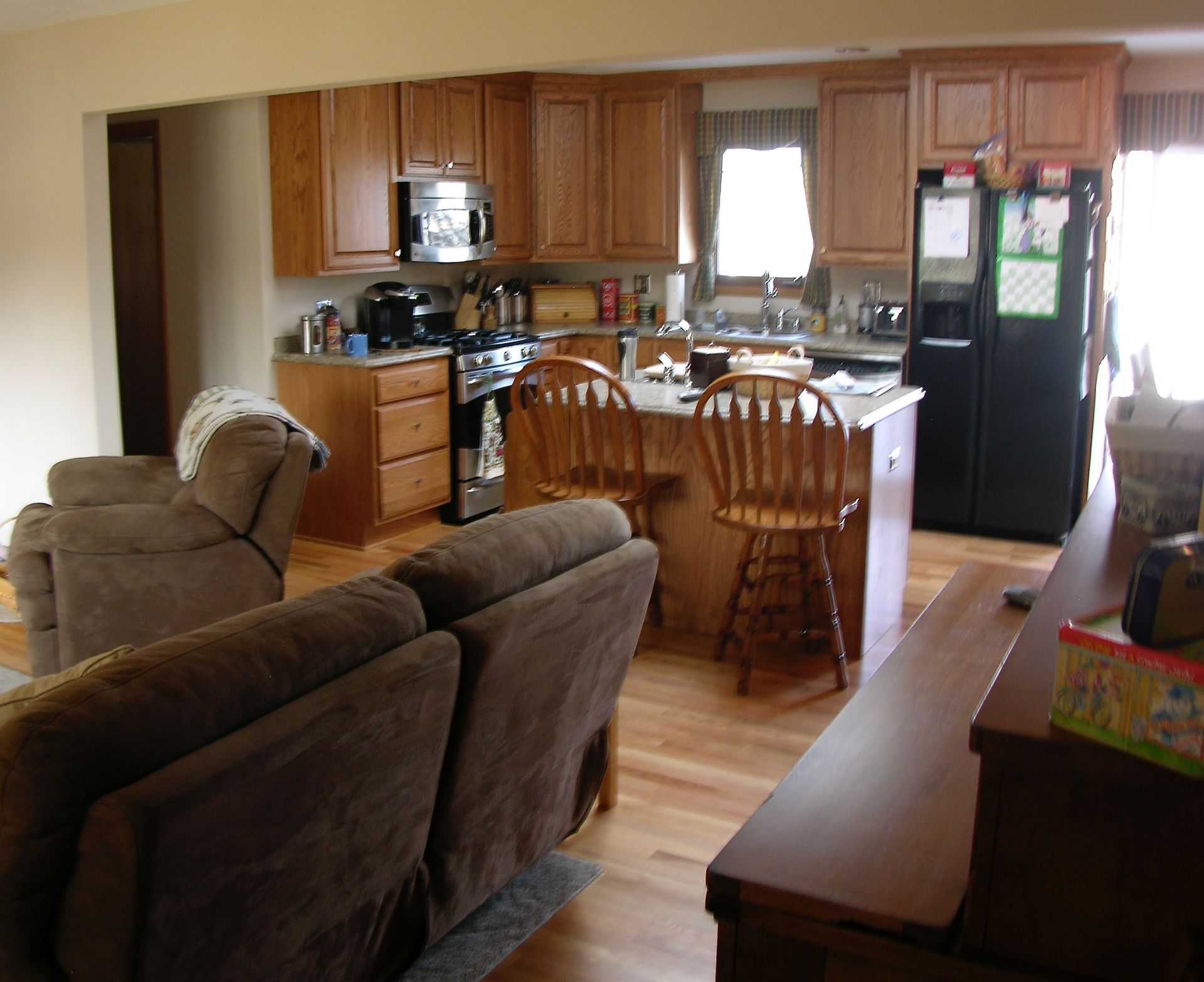 Kitchen with brown cabinets, island with stools, and dark fridge. Brown recliner in foreground.