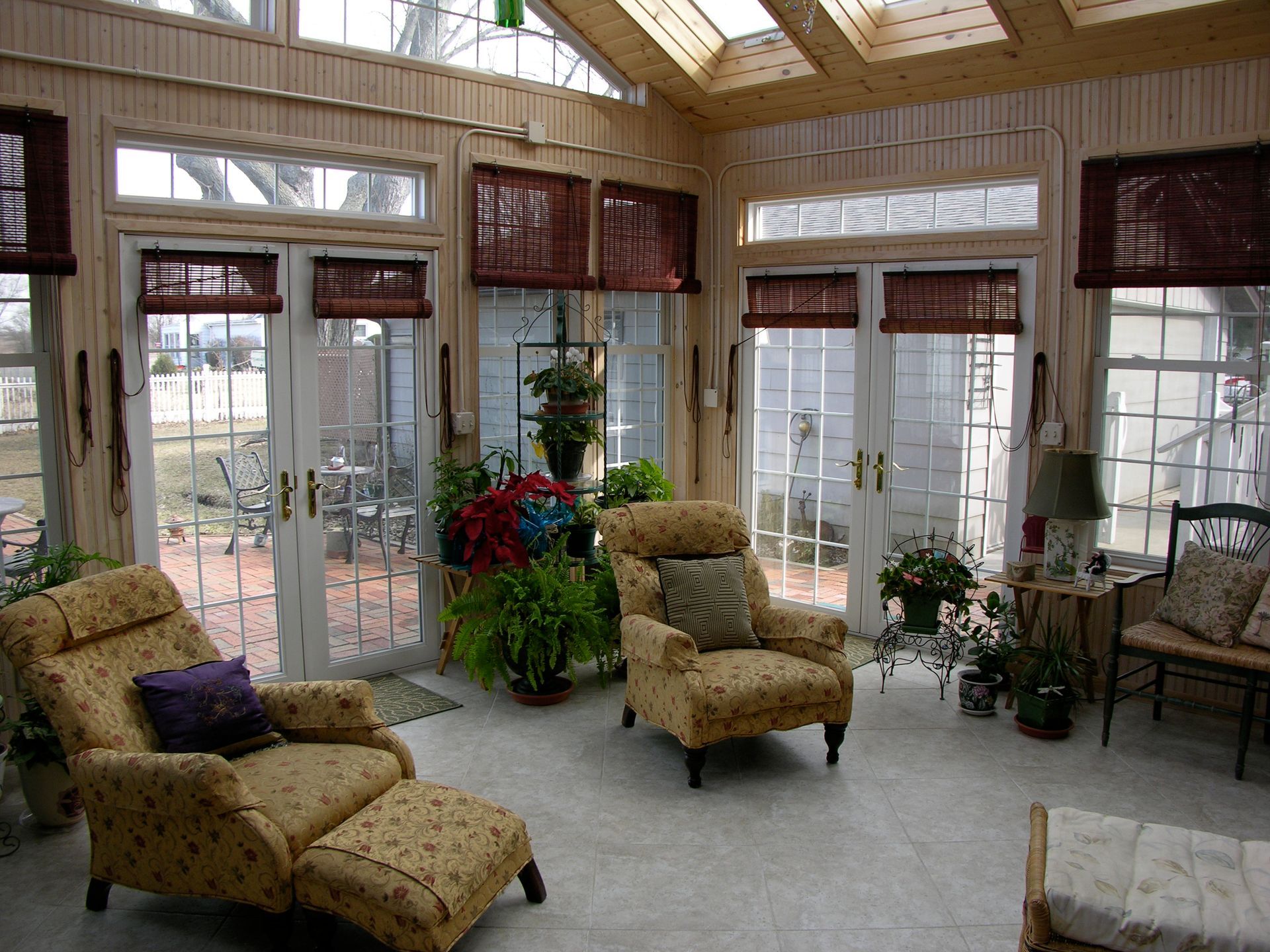 Sunroom interior with two armchairs, plants, and French doors leading to a backyard.