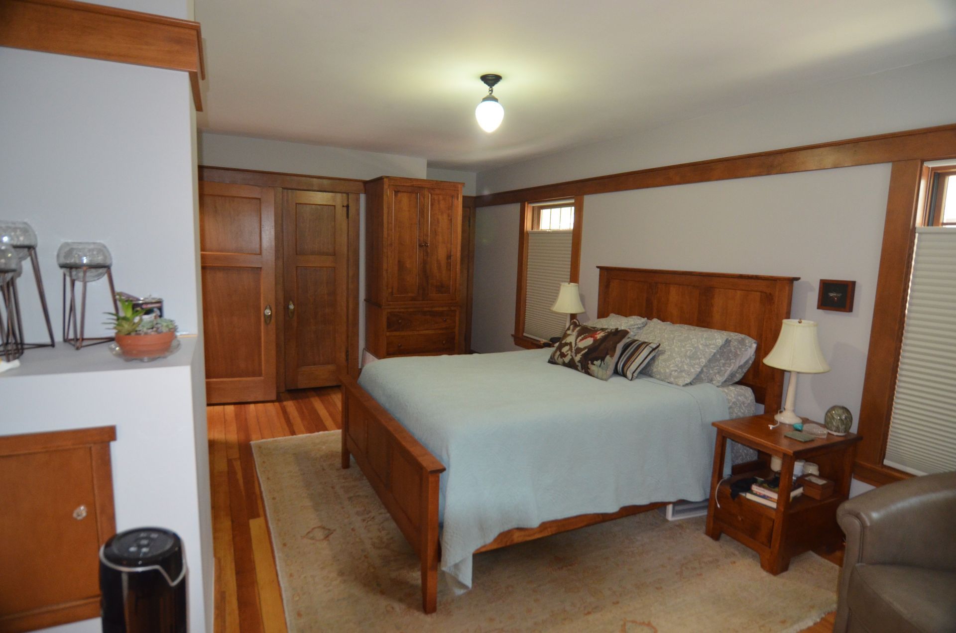 Bedroom with wooden furniture, including bed, nightstand, and wardrobe. Light blue bedspread and neutral rug.