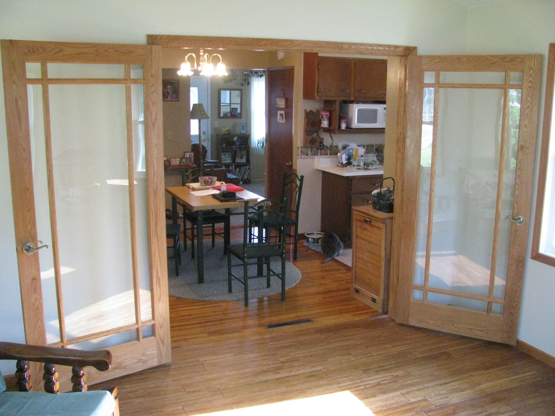Wooden-framed doors open to a dining room and kitchen, with a table, chairs, and cabinets visible.