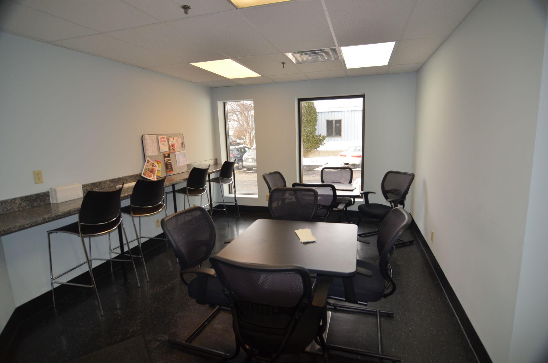 Meeting room with table, chairs, windows, and bar seating along a wall.