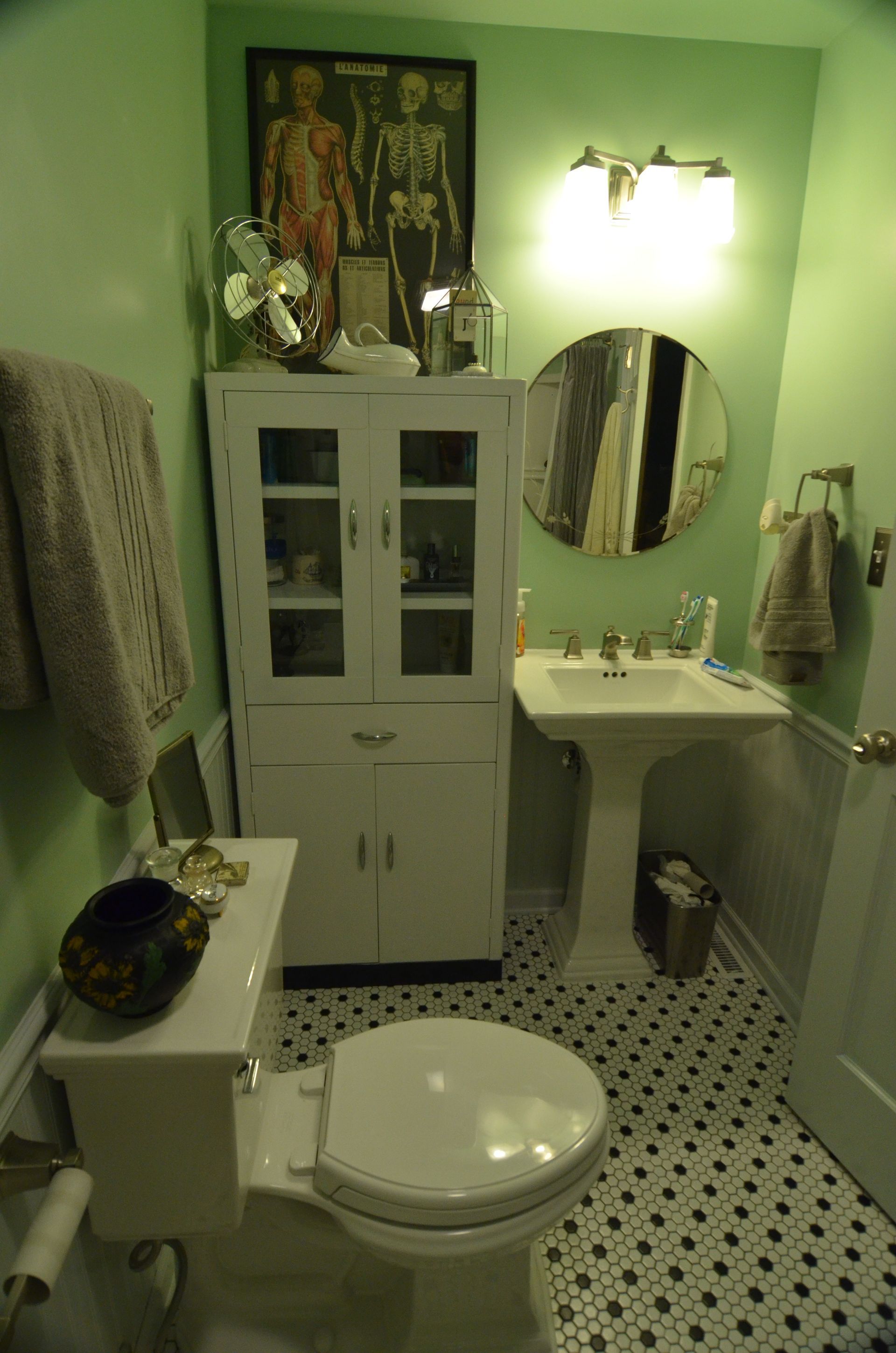 Small bathroom with a white toilet, pedestal sink, and white cabinet against green walls.