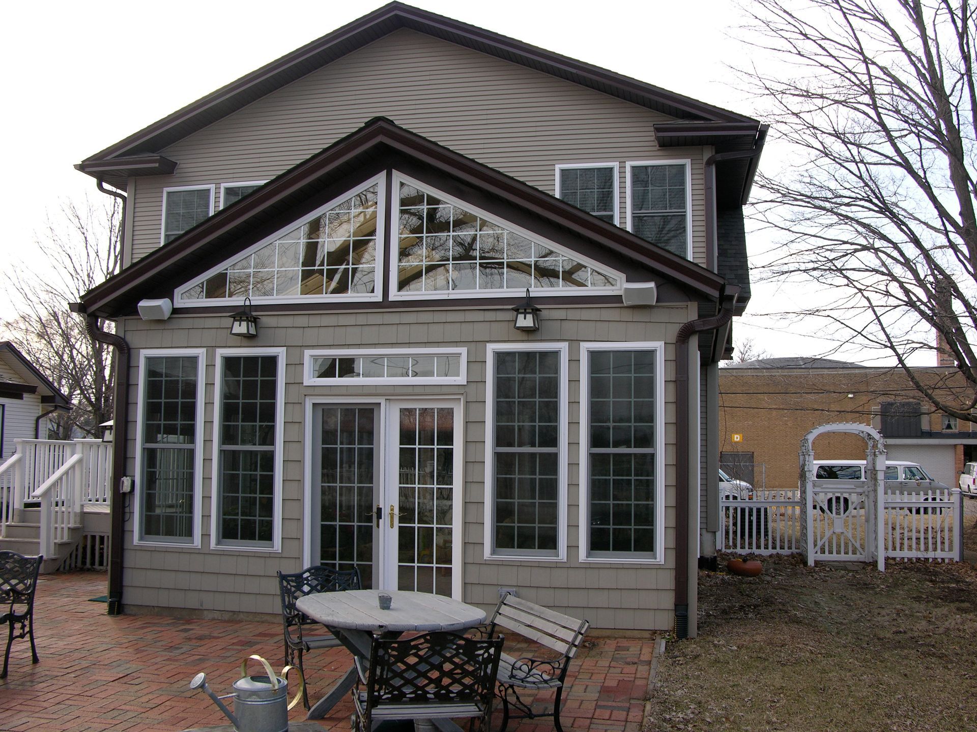 Tan house with sunroom, glass windows, brick patio, and outdoor furniture.
