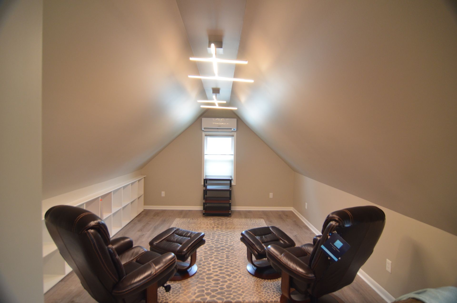 Attic room with two brown leather recliners, an area rug, and linear ceiling lights.