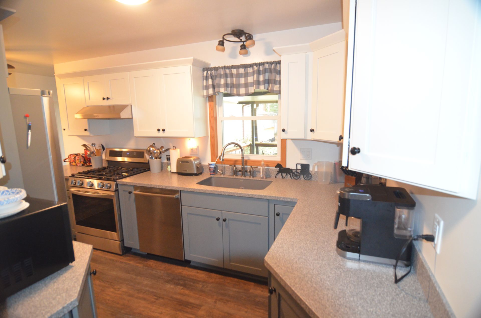 Kitchen with white cabinets, gray countertops, stainless steel appliances, and a window with a plaid valance.