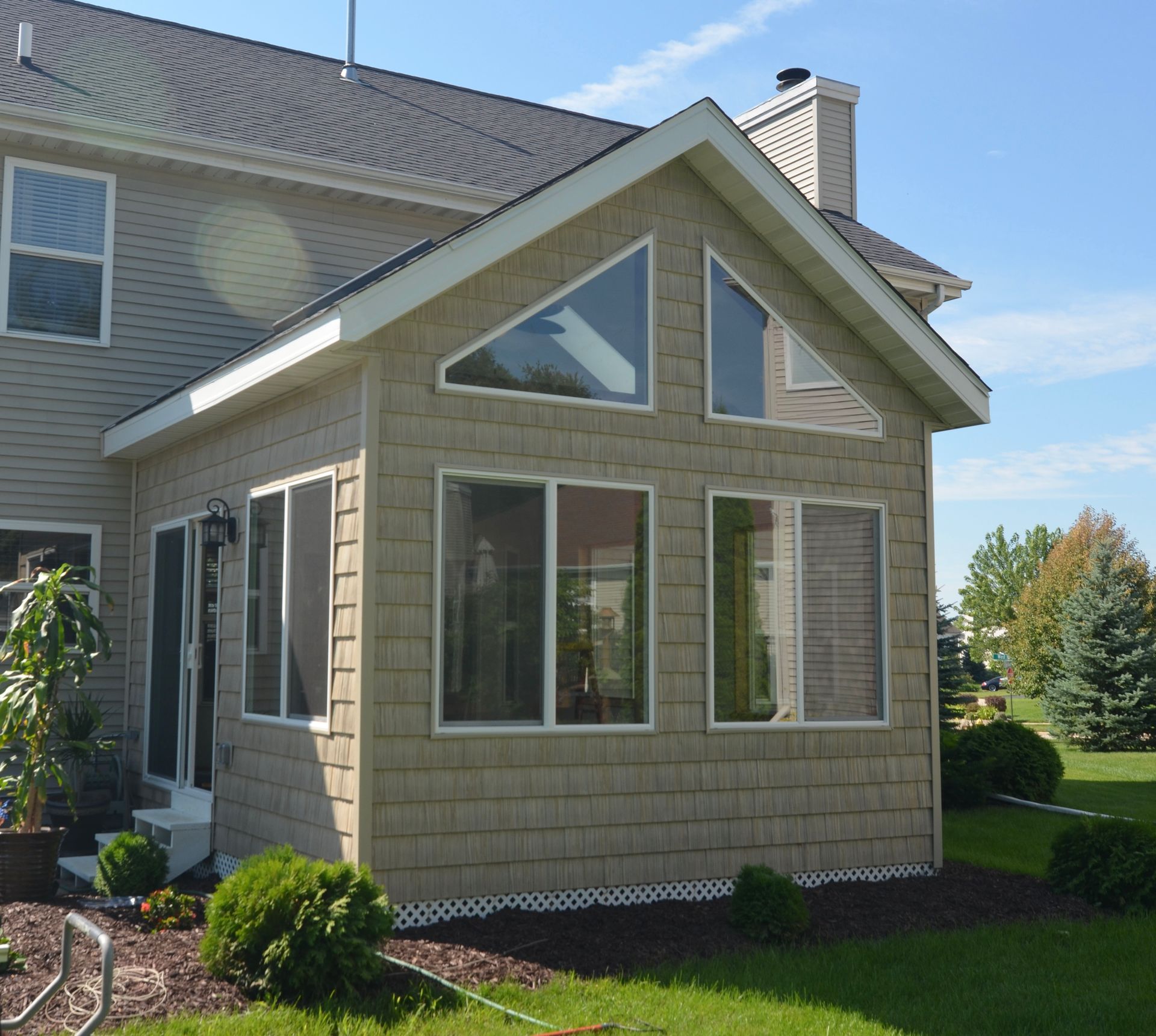 Sunroom addition with tan siding, windows, and angled roof, attached to a house.