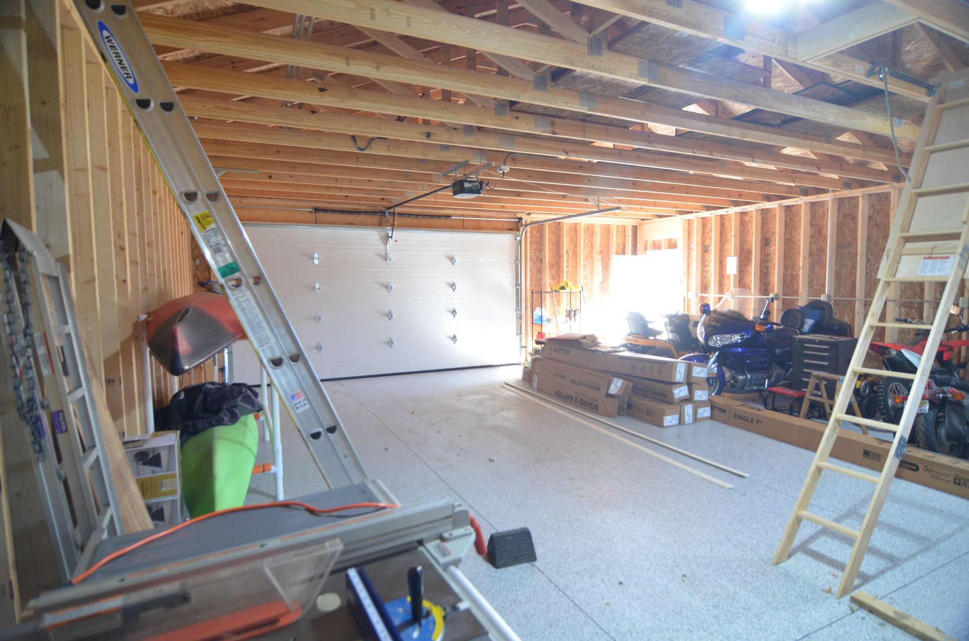 Interior view of a wooden garage under construction, with a closed garage door and building materials.