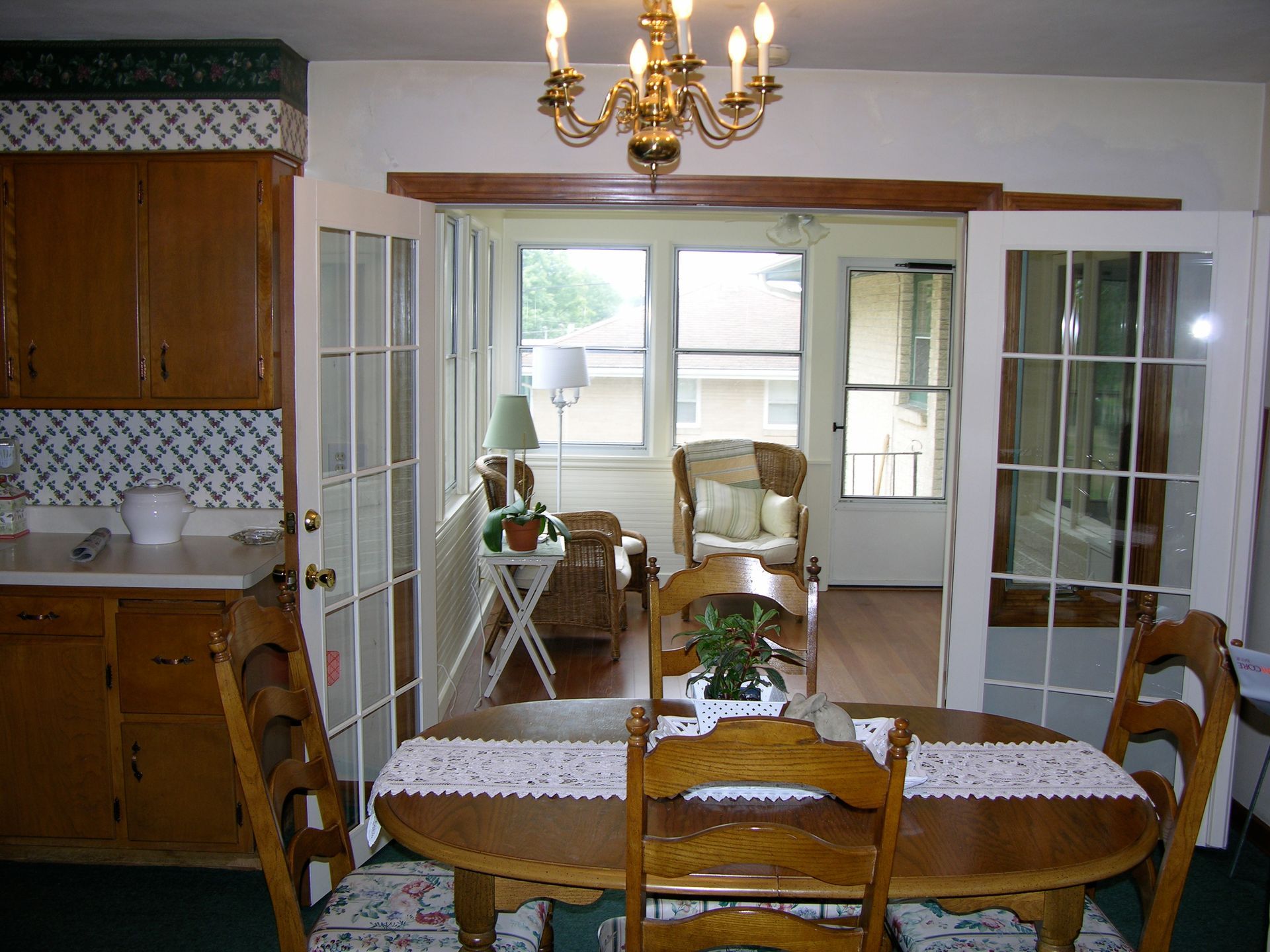 Dining room with wooden table and chairs, French doors leading to a sunroom, and a chandelier.