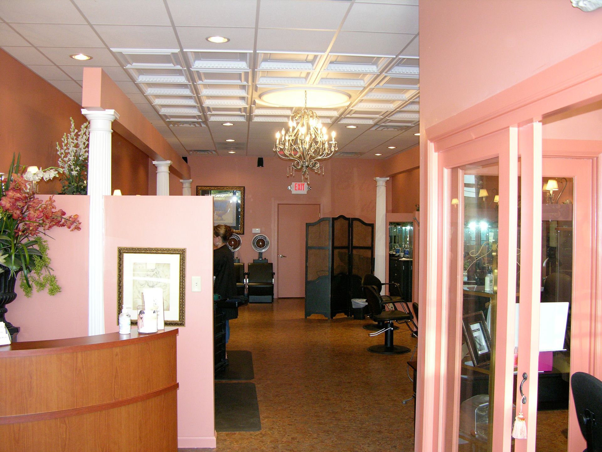 Interior of a pink hair salon with a reception desk, a chandelier, and a decorative ceiling.