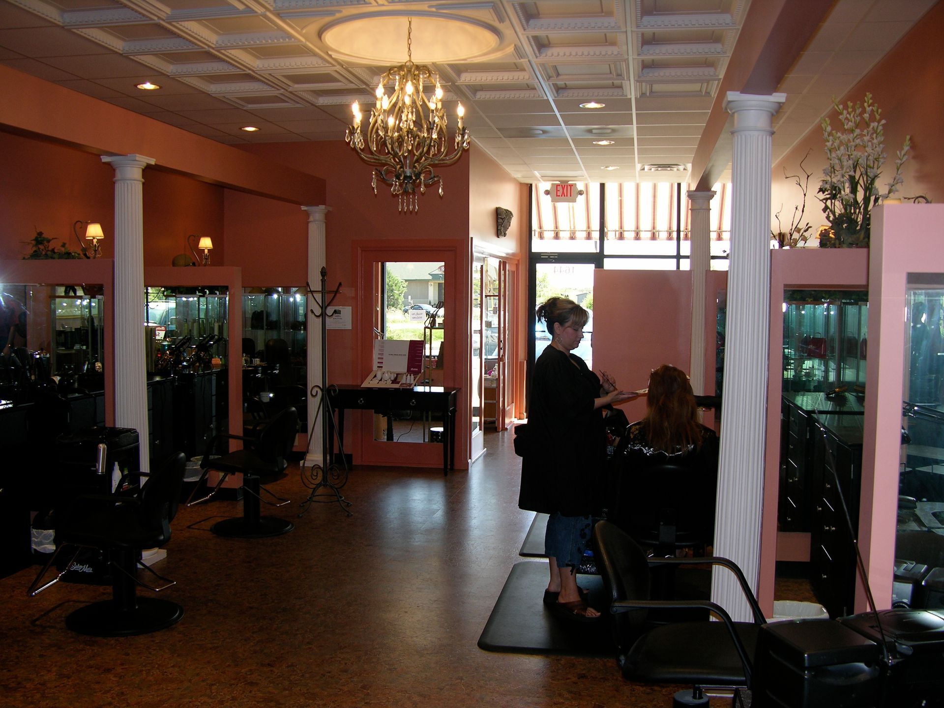 Hair salon interior with stylist working on a client's hair. Pink walls, columns, chandelier.