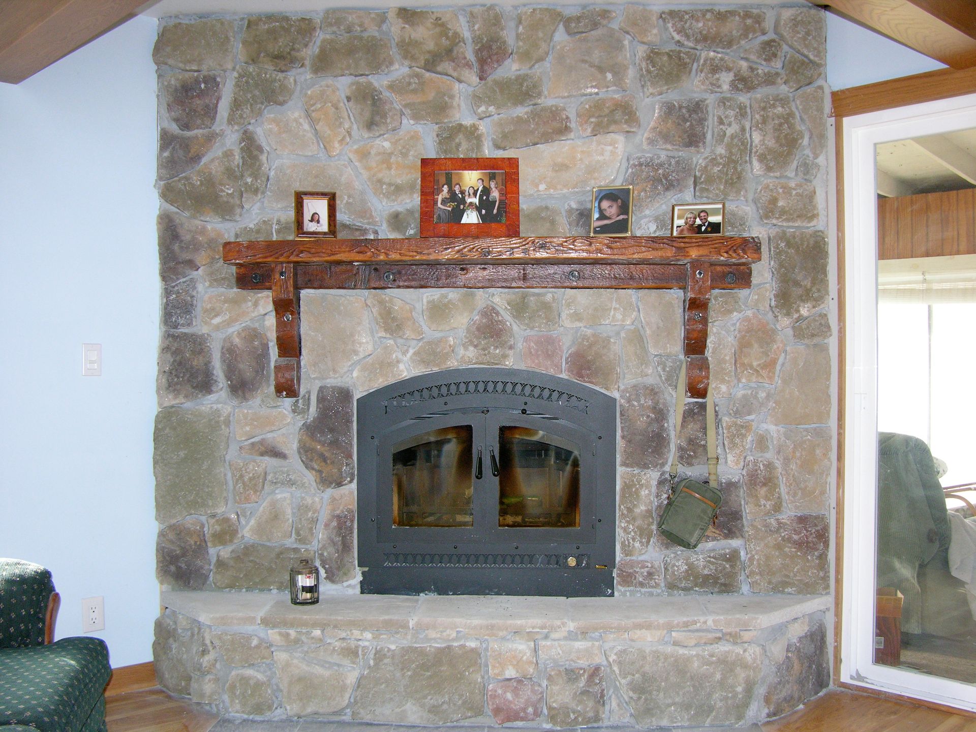 Stone fireplace with wood mantel, decorative brackets, and a black insert, with photos and a candle.