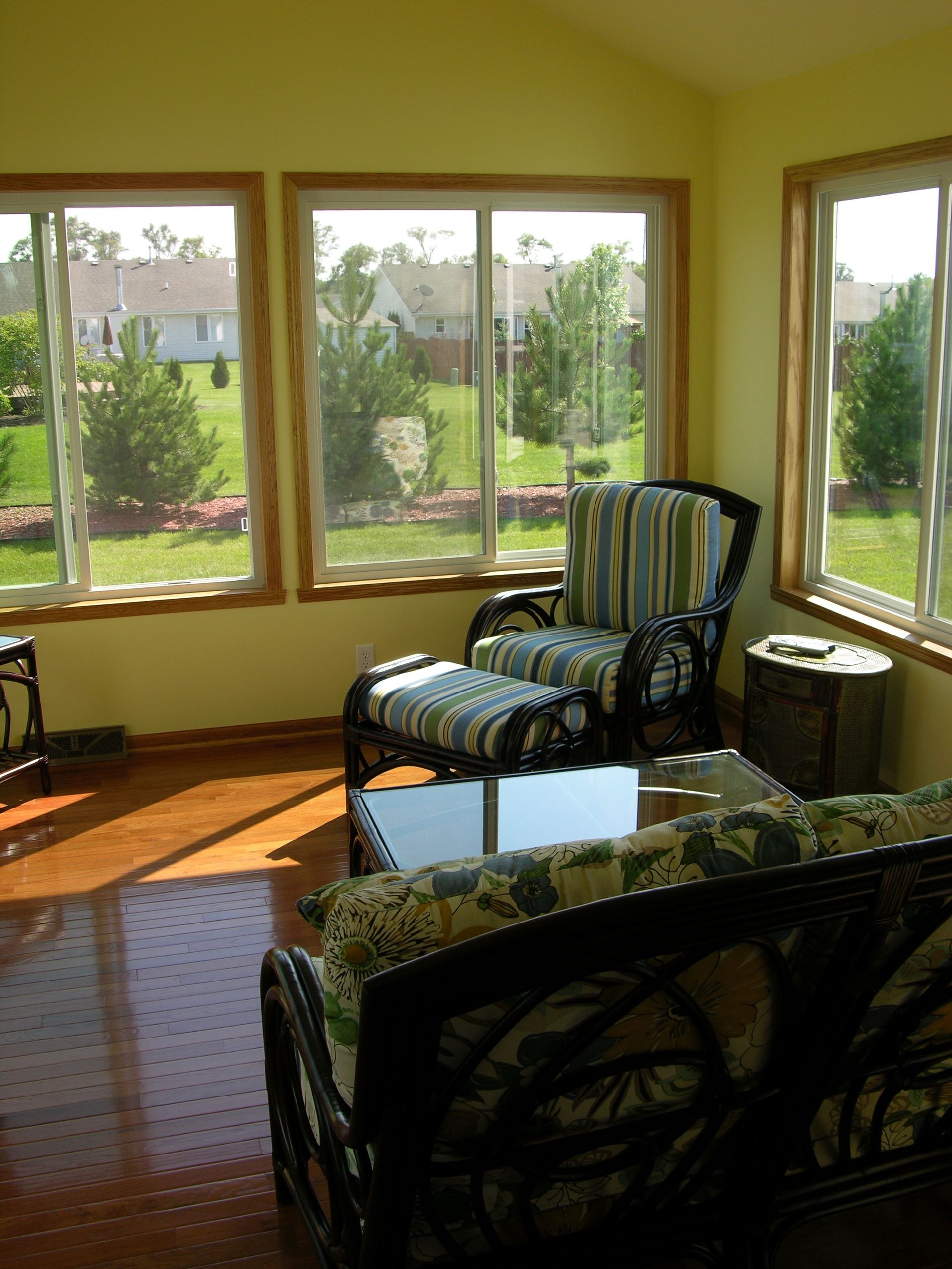 Sunroom with wicker furniture, windows, and a view of a green yard and houses.