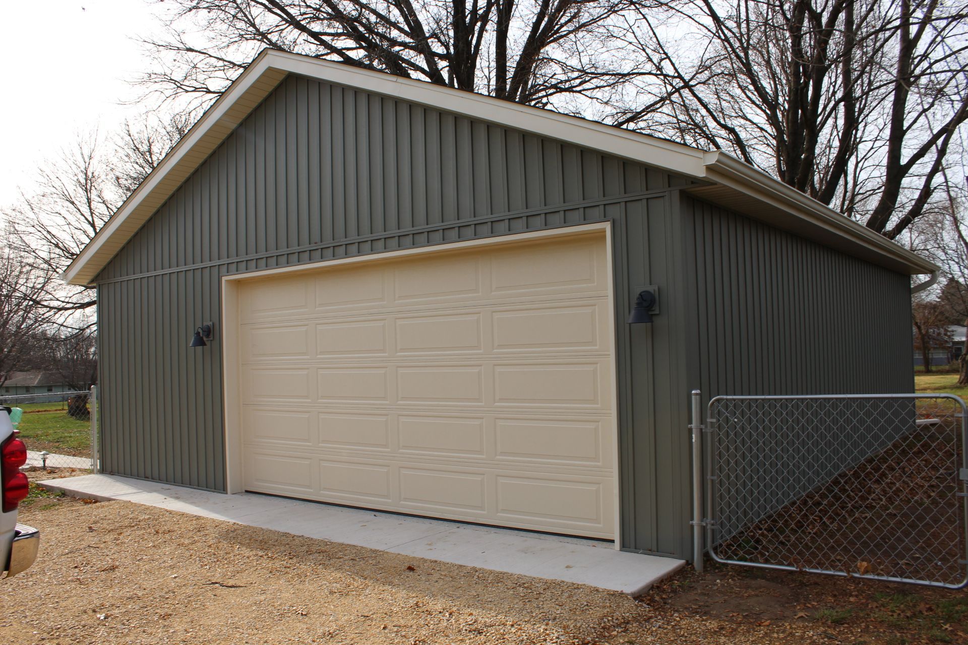 Green and beige garage with an open door, a concrete pad, and a chain-link fence.