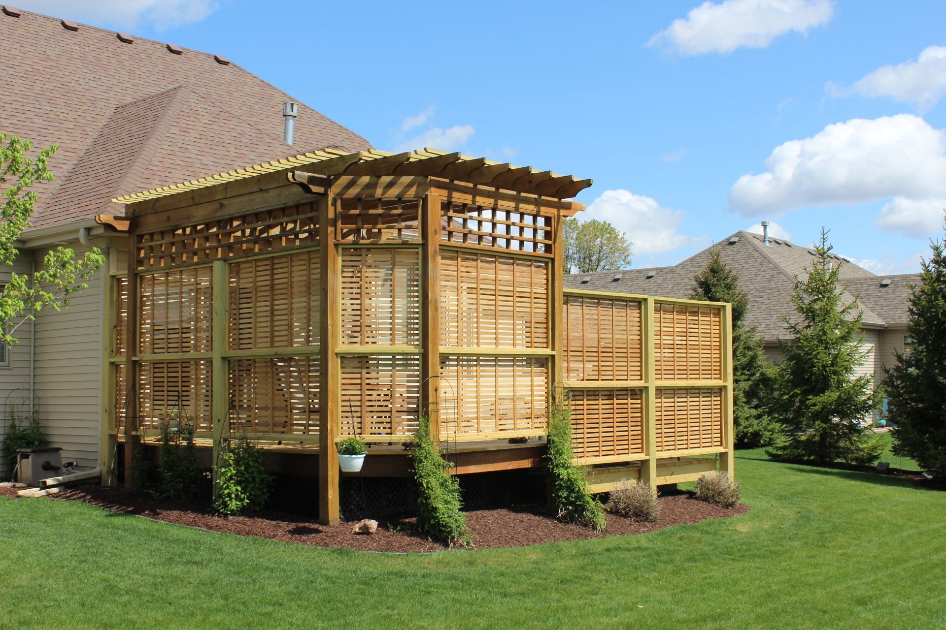 Wooden deck with latticed walls and a pergola in a sunny backyard.