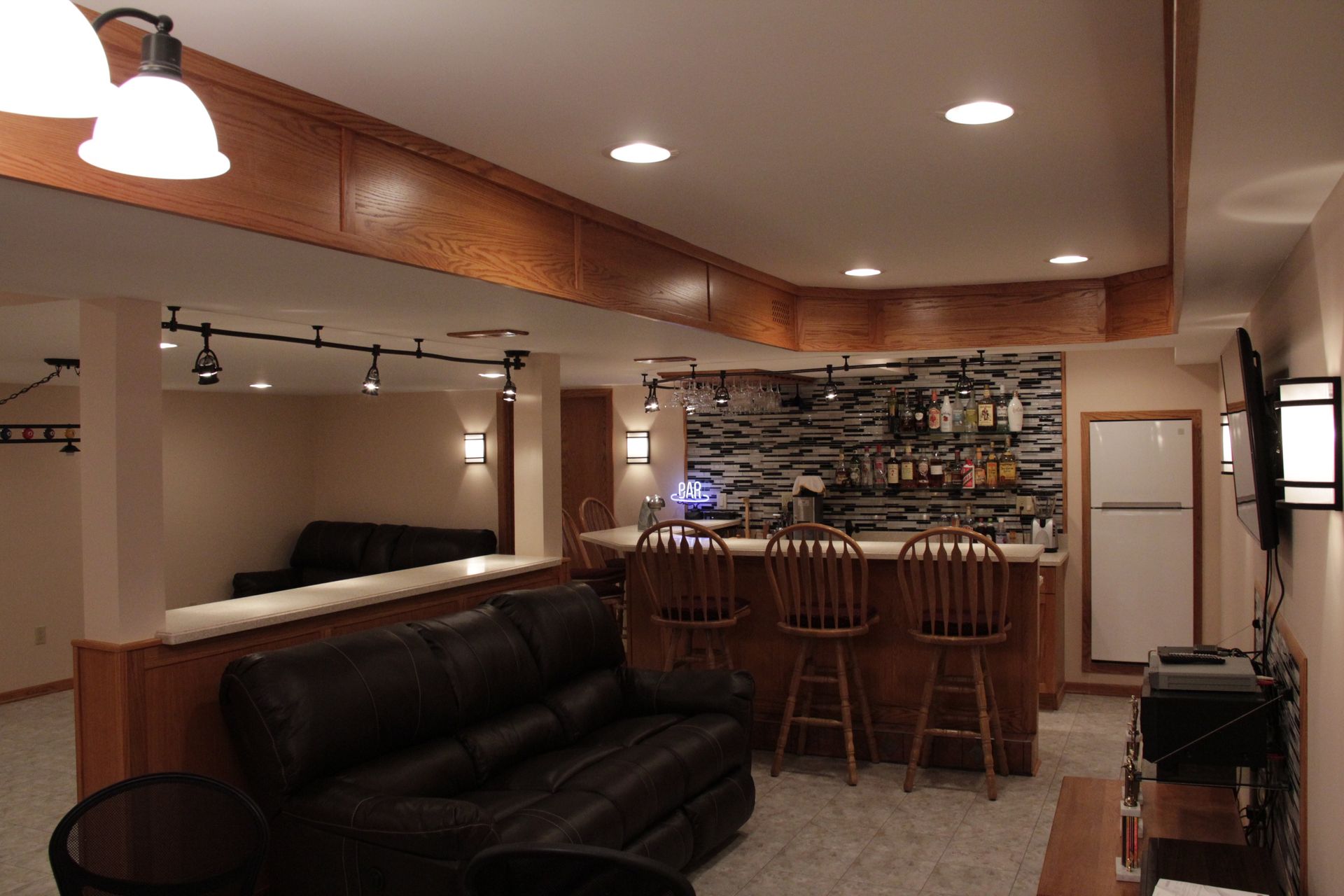 Basement bar with dark leather couches, wooden bar, and stone backsplash.