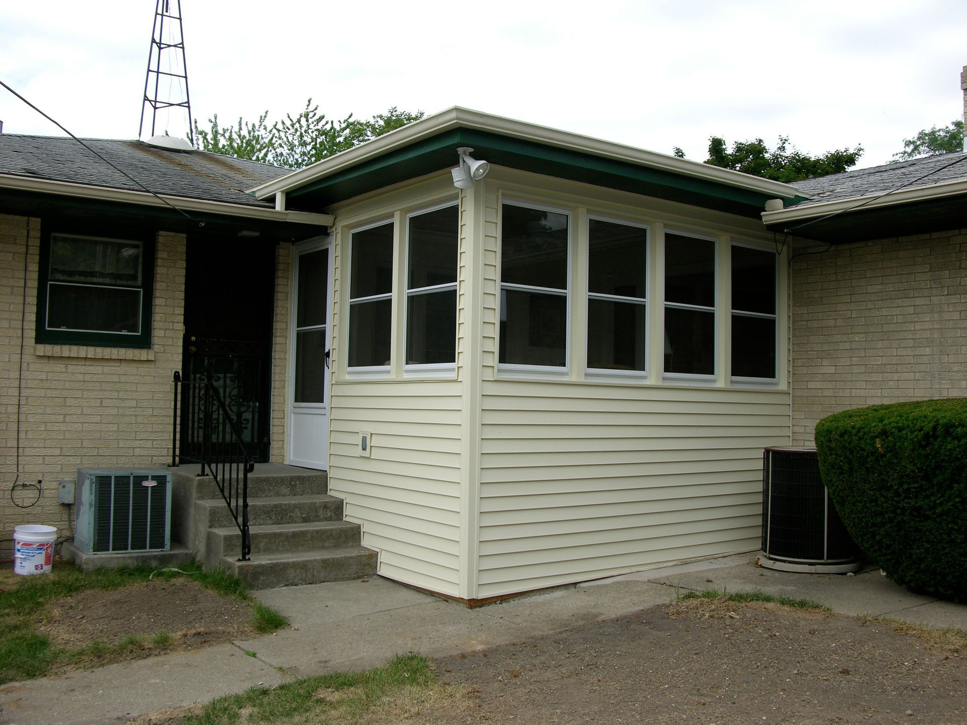 Exterior view of a house with a sunroom, brick walls, and concrete steps leading to the door.