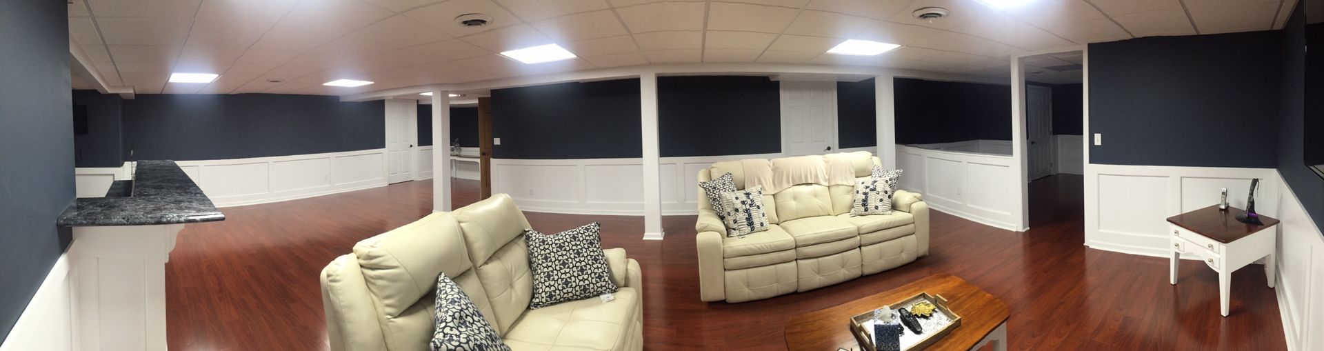 A finished basement with two beige sofas, dark wood floors, white trim, and dark walls.