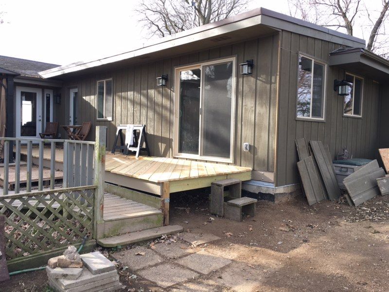 Exterior of a house with a wooden deck, sliding glass door, and green siding.