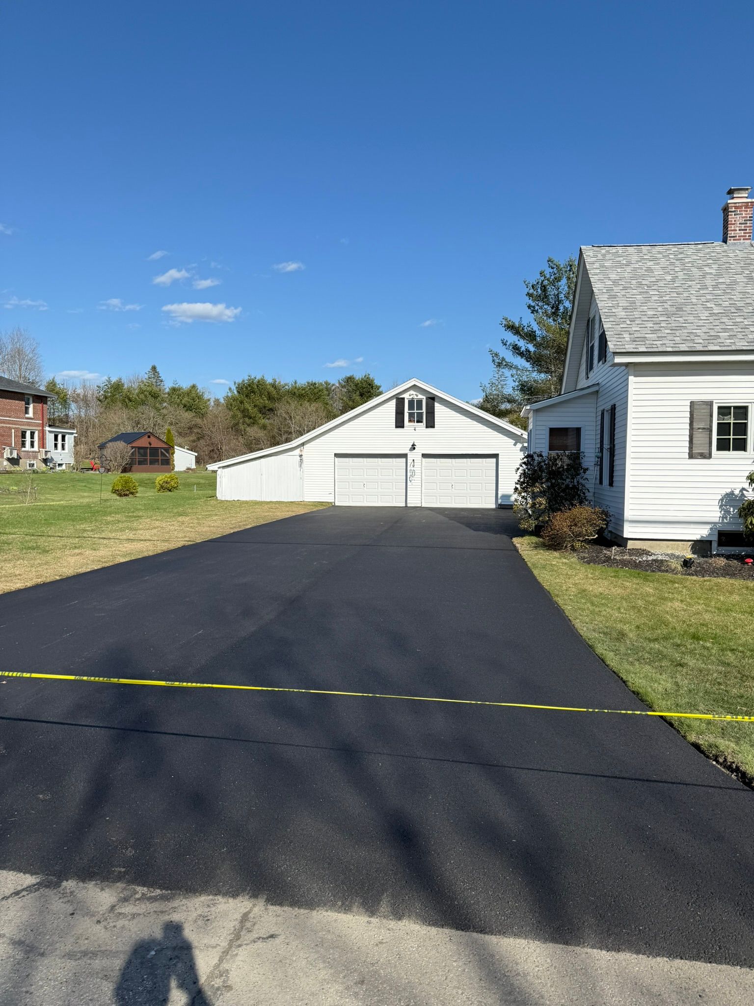 A freshly paved asphalt driveway leads to a two-car garage beside a white house on a sunny day.