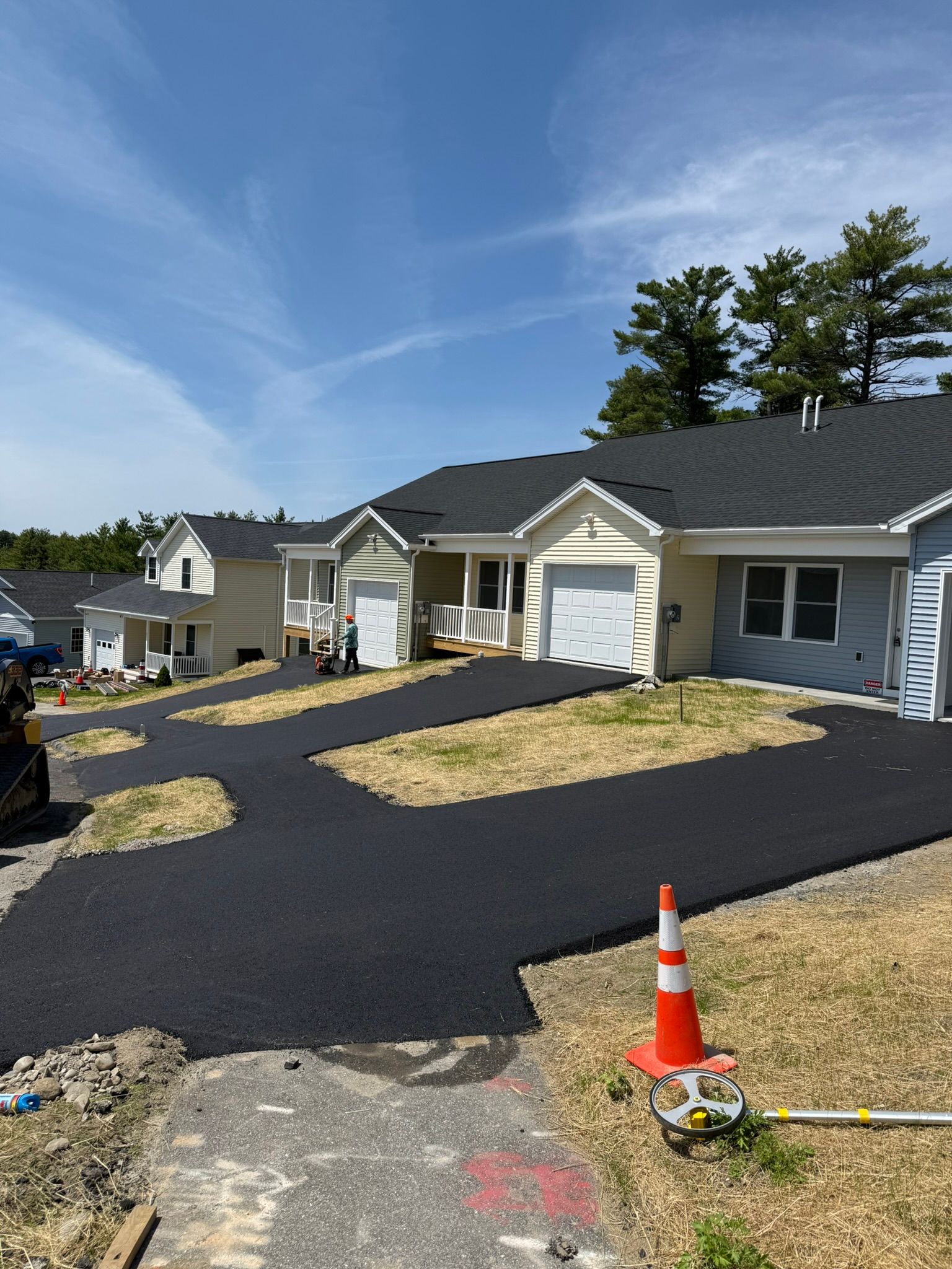Newly paved black asphalt driveways connecting to garage entrances of light-colored suburban houses under a blue sky.
