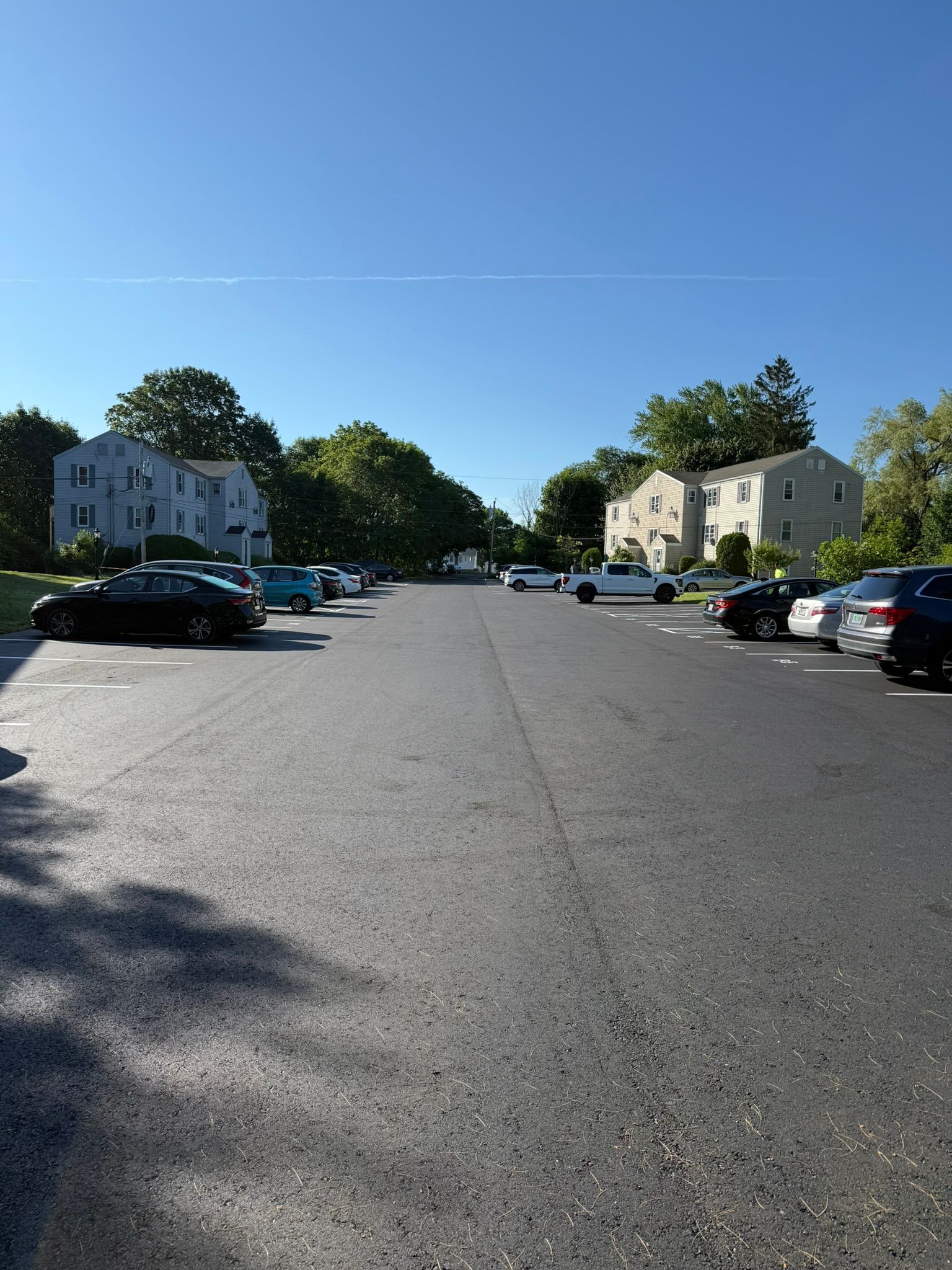 Parking lot between two apartment buildings on a clear day with several parked cars.