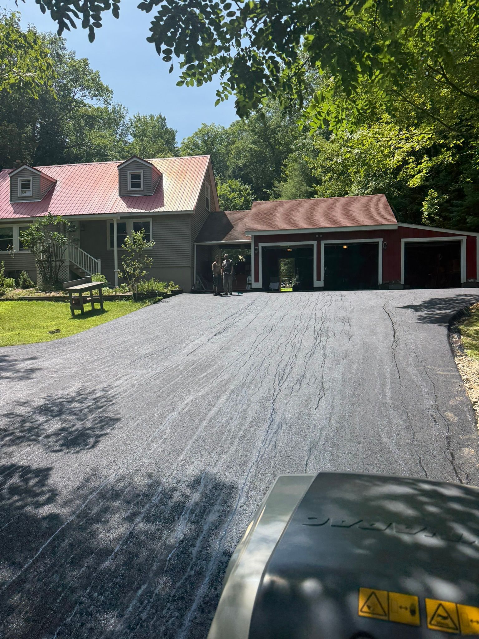 A freshly laid gravel driveway leads toward a house with a red roof and an attached three-car garage.