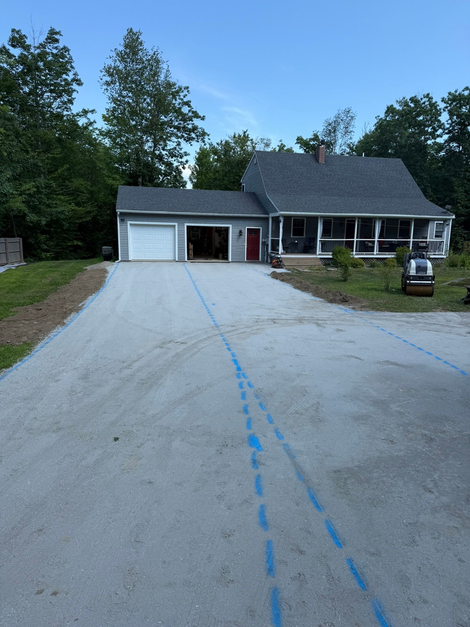 A gravel driveway leads to a house with a garage and porch, featuring blue painted guide lines on the ground.