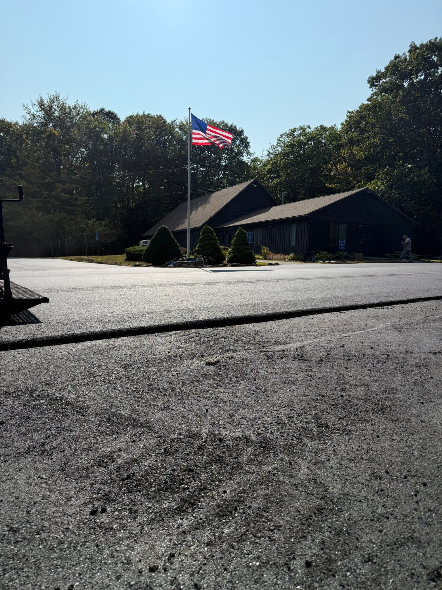 An American flag waves on a tall pole in front of a dark-colored house set against a background of green trees.