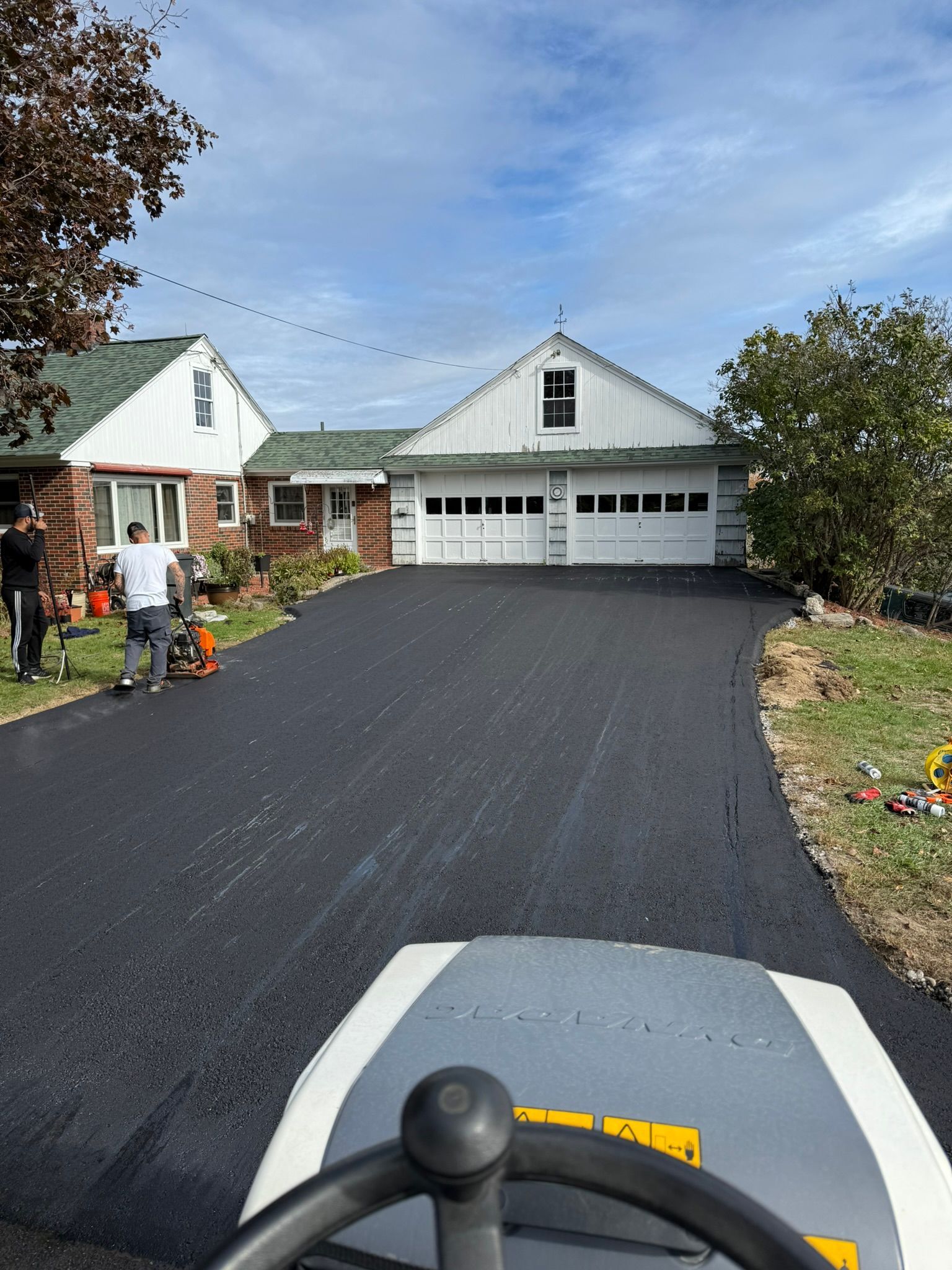 View from a roller cab showing workers paving a driveway leading up to a house with a two-car garage.