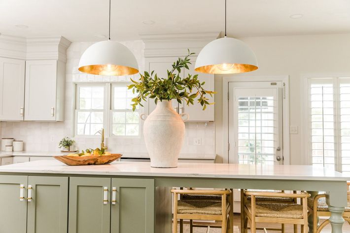 A kitchen with green cabinets , white counter tops , and a large island with a vase of flowers on it.