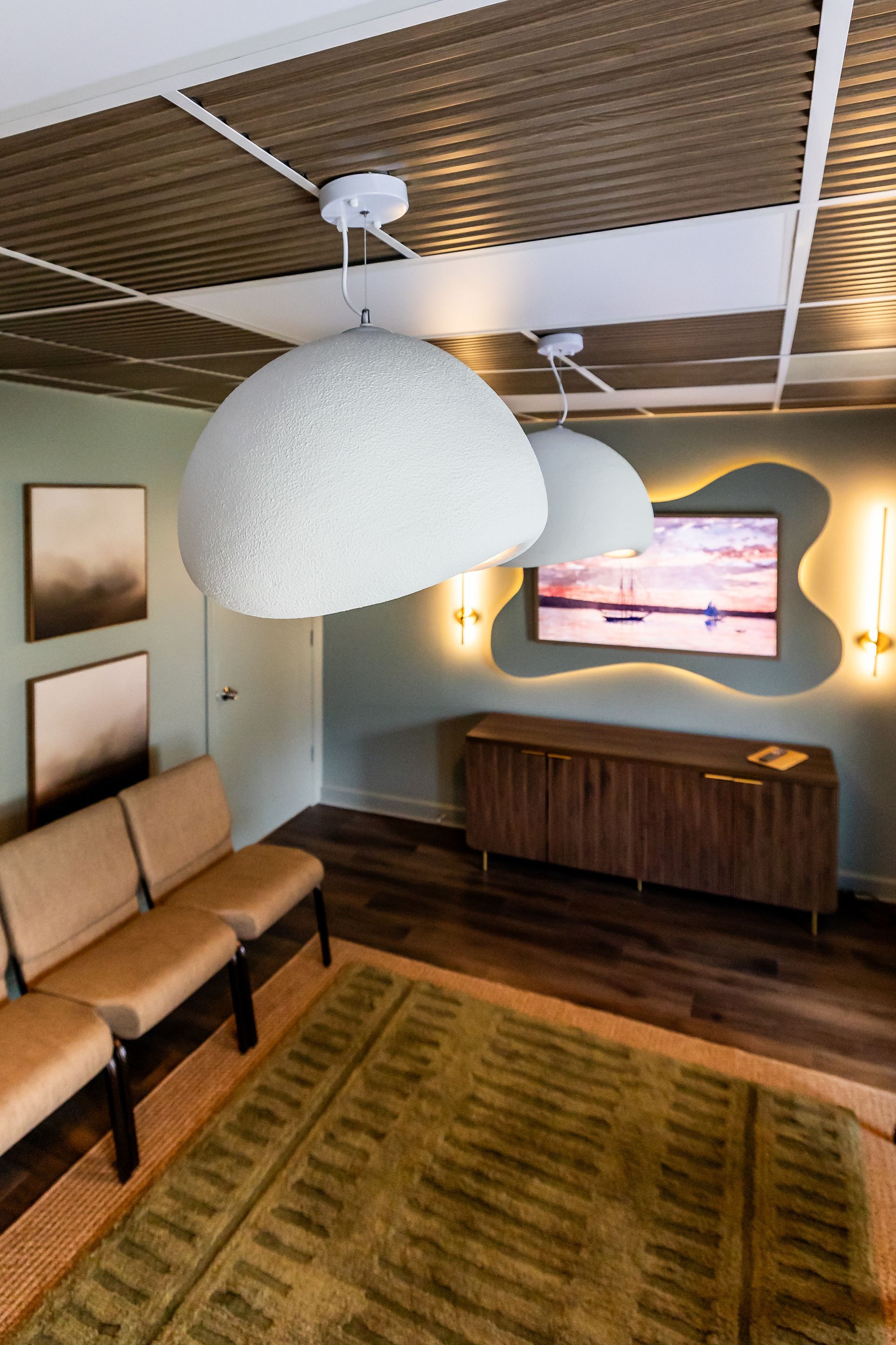 Cozy waiting room with white lamps, green rug, tan seating, and wooden console below TV with an orange outline.