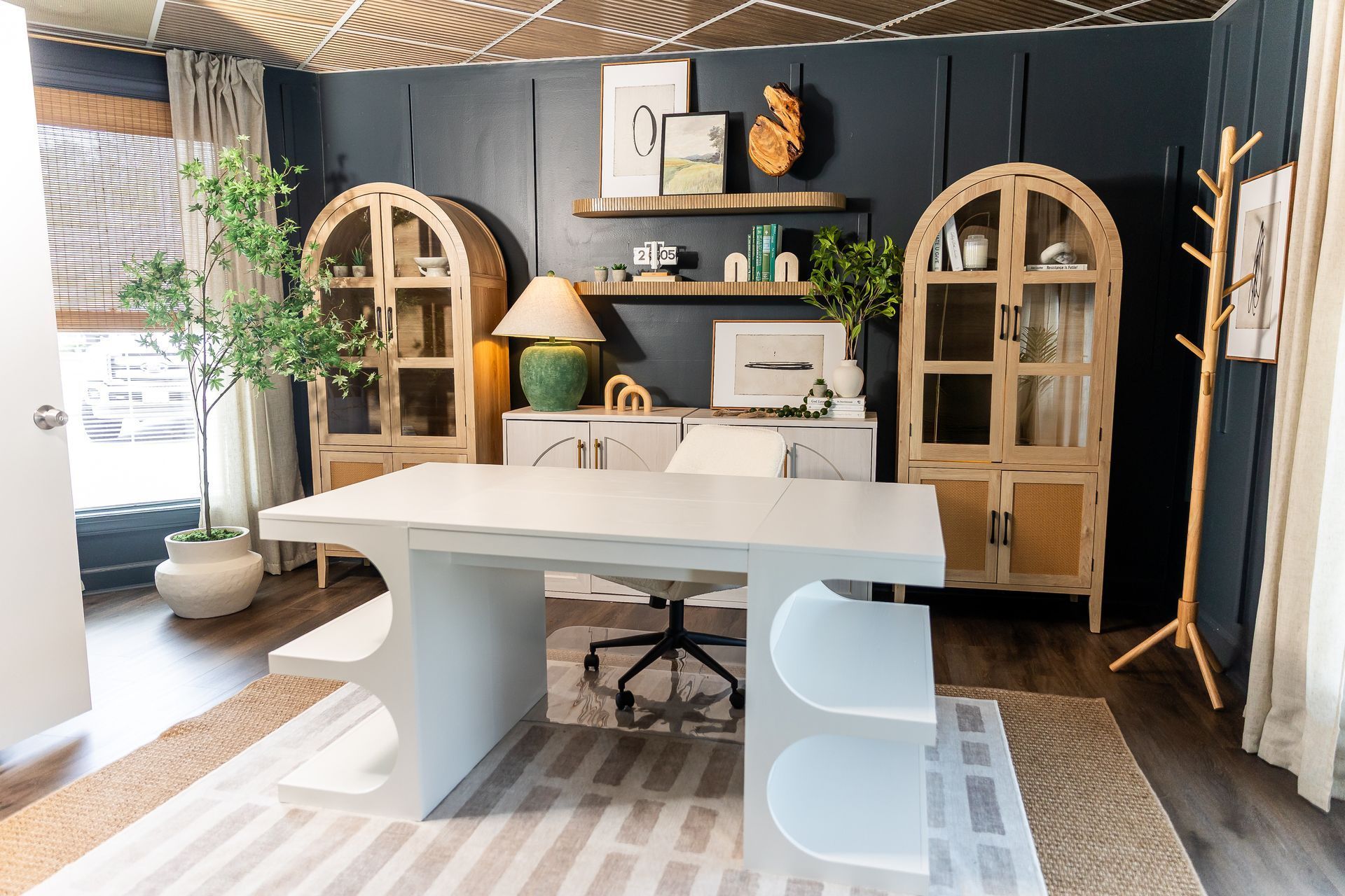 Home office with blue wall, white desk, light brown cabinets, and green plant.