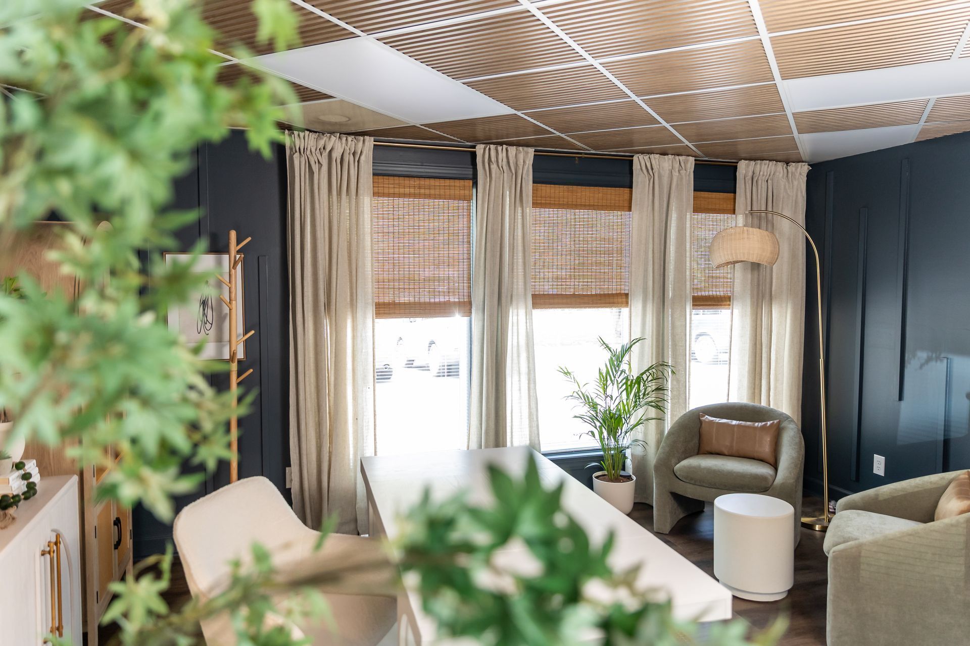 Cozy room with windows, beige curtains, and a patterned ceiling. Green plants and soft seating create a relaxing atmosphere.