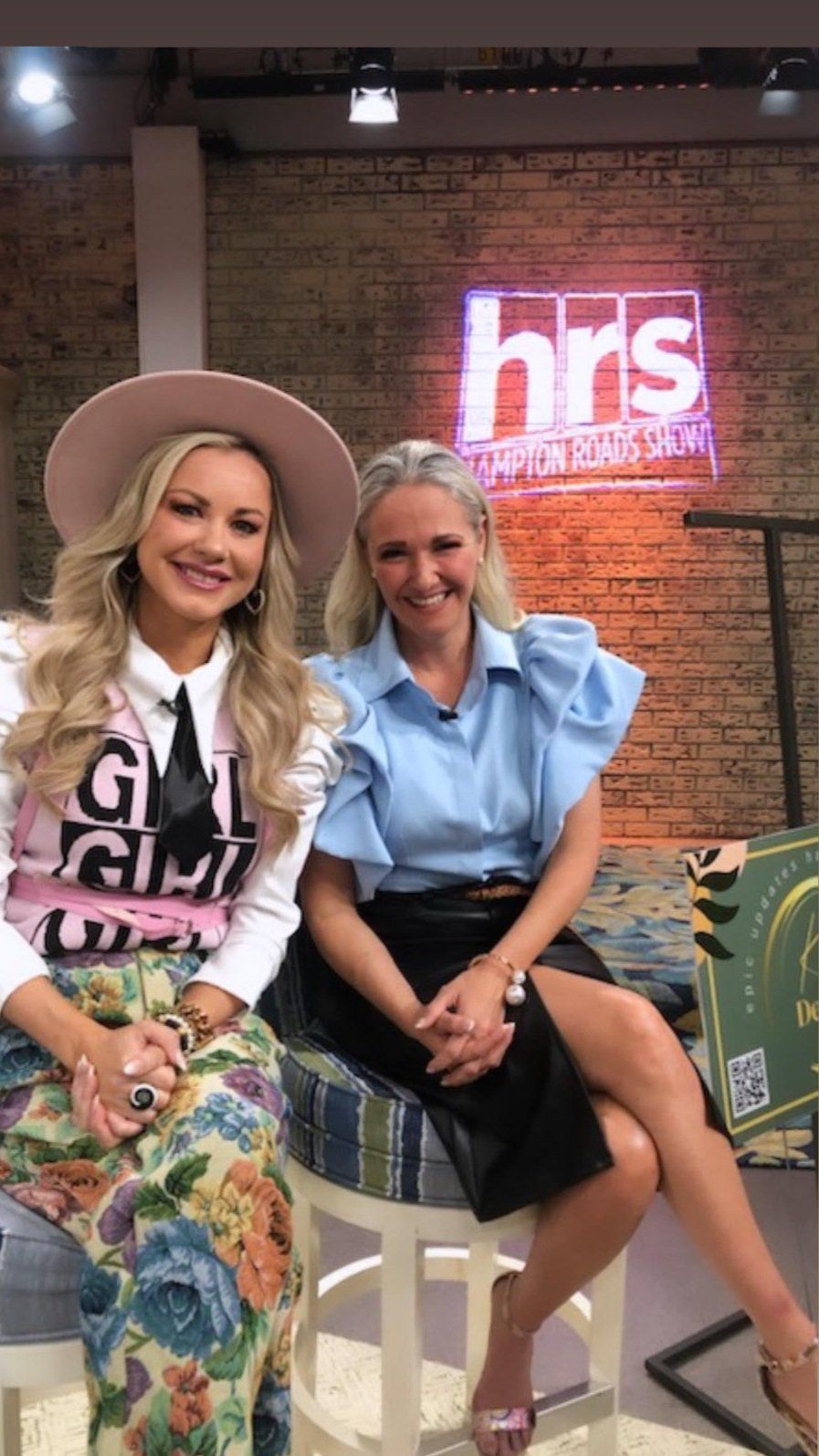 Two women are sitting next to each other in front of a sign that says hrs.