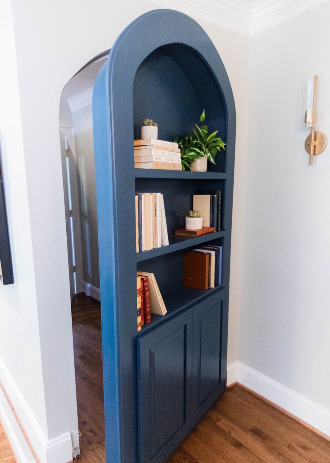 A blue bookshelf with books and plants on it in a hallway.