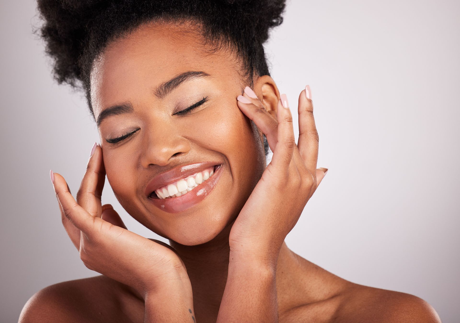 A woman is smiling and touching her face with her hands.