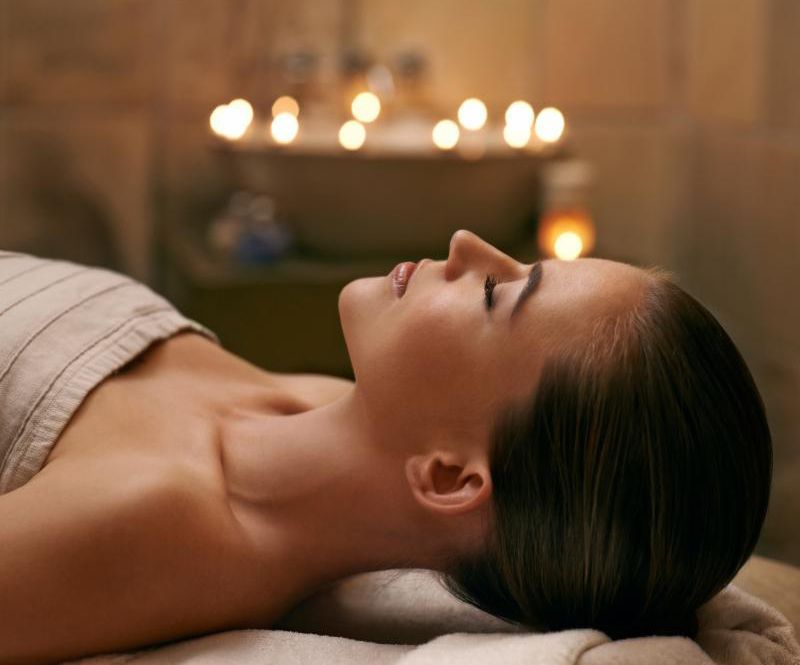 Woman lying on a spa table during a facial treatment with candles glowing in the background