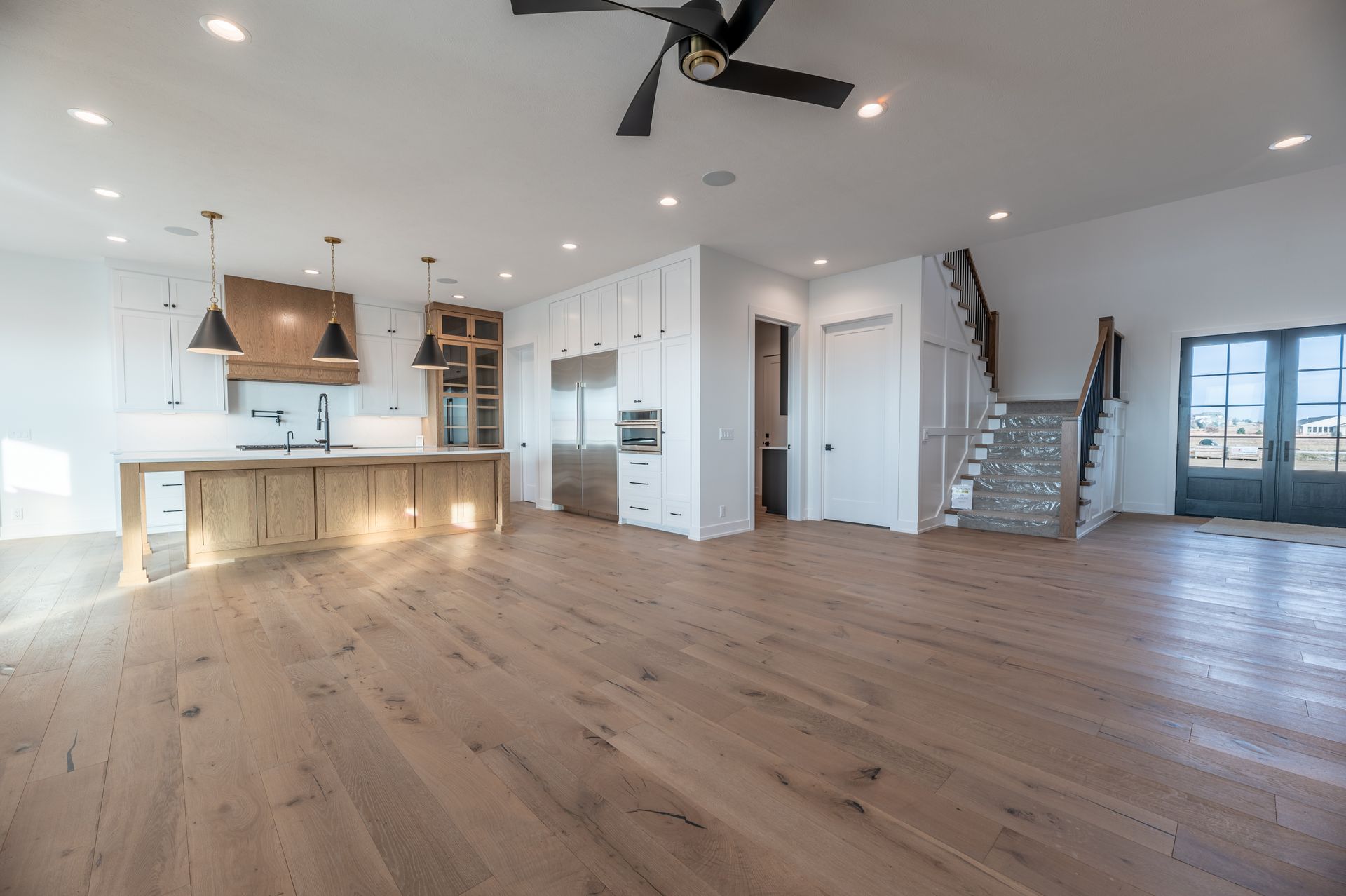 Spacious open-concept kitchen with light wood floors, white cabinets, and a rustic wooden range hood.