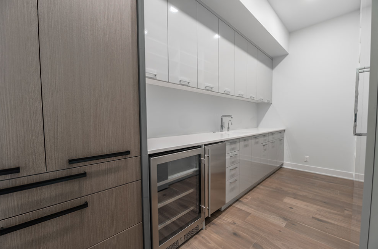 A pantry with light wood cabinets, stainless steel appliances, and a wine cooler.