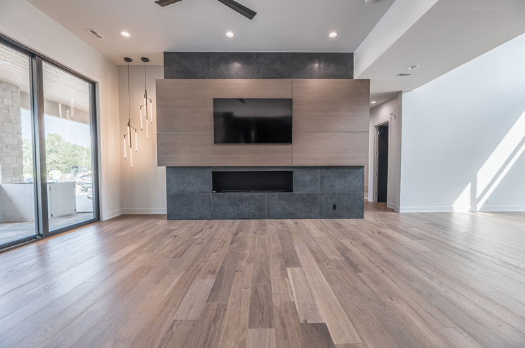 Empty modern living room with wood floors, fireplace, TV, and large sliding doors.