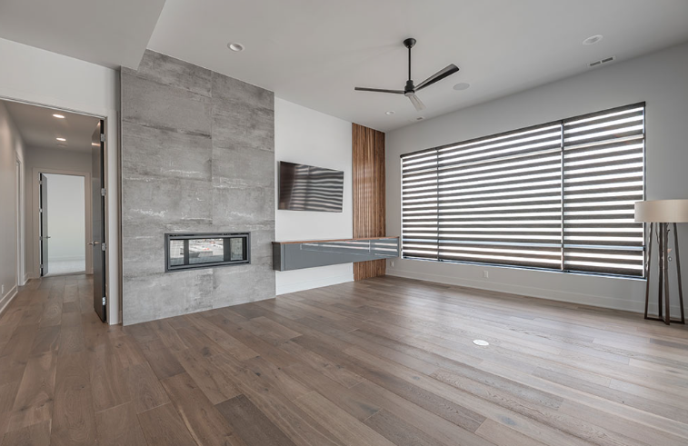 Modern living room with fireplace, gray wall, wood floor, large window with blinds.