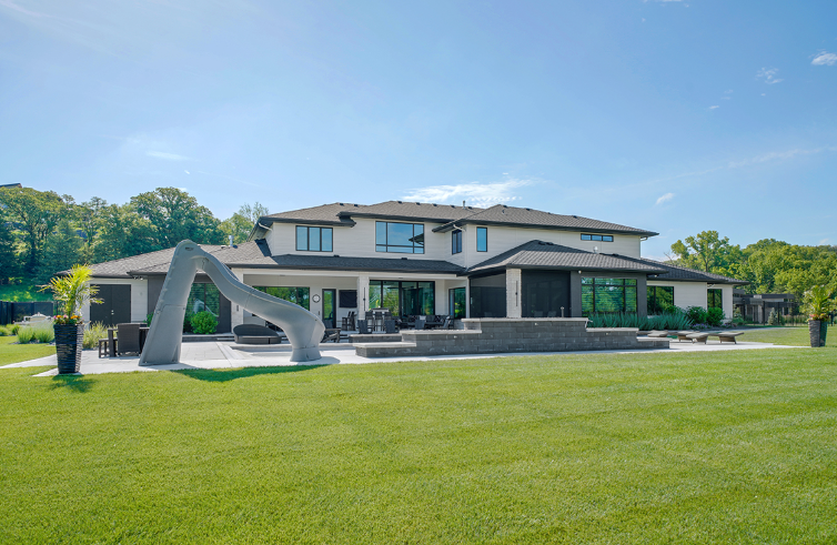 Large white house with extensive lawn, modern sculpture, and blue sky.