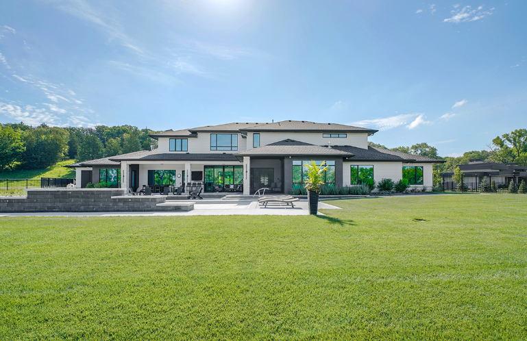 Large, modern house exterior with expansive green lawn and blue sky.